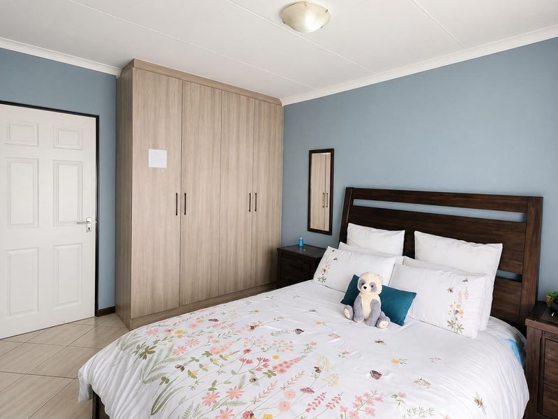 A well-maintained bedroom featuring built-in wooden cupboards, tiled flooring, and neutral blue wall finishes.