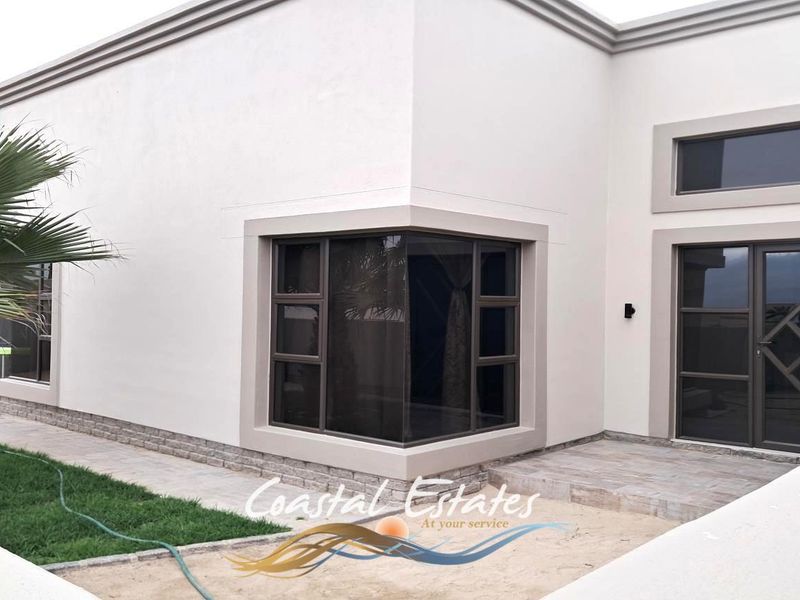 A modern exterior view of the property featuring clean white walls, stone cladding accents, and dark aluminium window and door frames.