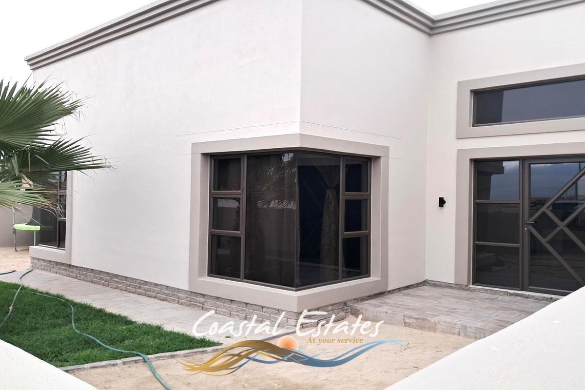 A modern exterior view of the property featuring clean white walls, stone cladding accents, and dark aluminium window and door frames.