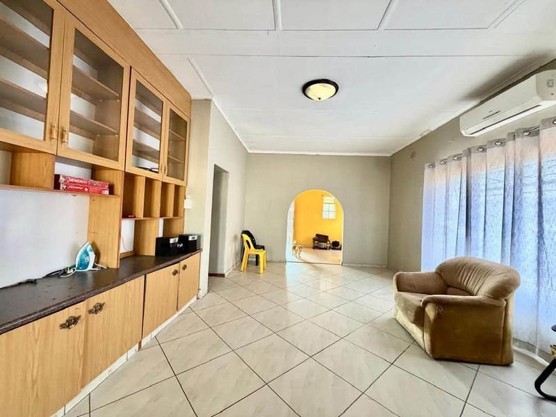 Spacious living area featuring built-in wooden cabinetry, tiled flooring, and an arched entryway leading to an adjacent room.