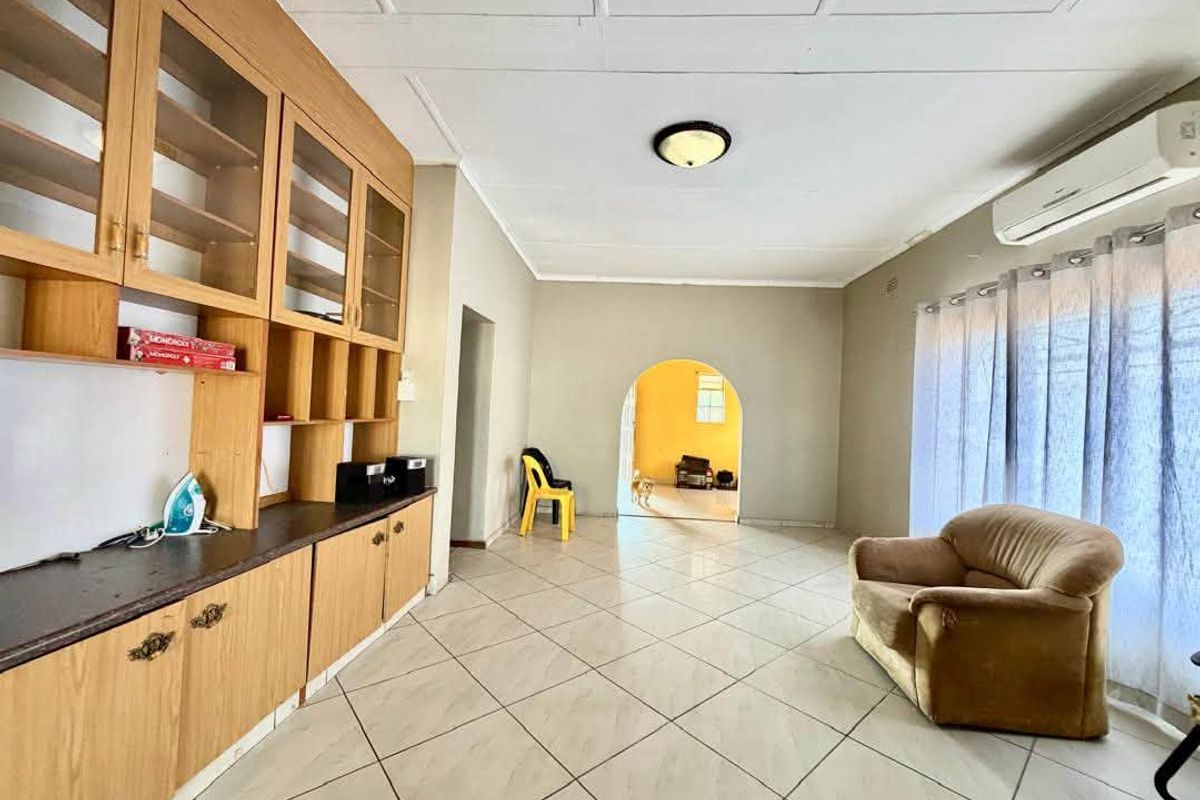 Spacious living area featuring built-in wooden cabinetry, tiled flooring, and an arched entryway leading to an adjacent room.