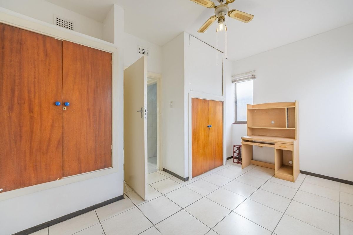 A bedroom featuring tiled flooring, built-in wooden cupboards, and a ceiling fan, offering a functional space with potential for modern updates.