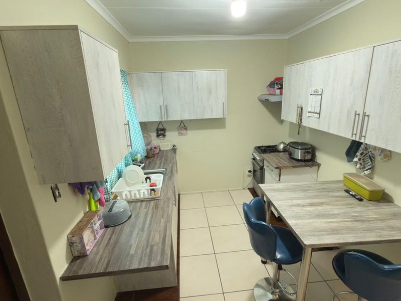 A functional kitchen featuring light wood-grain cabinetry, laminate countertops, a gas stove with extractor fan, and tiled flooring.