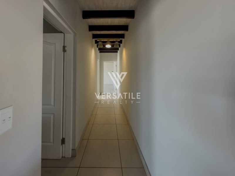 A clean, well-lit hallway featuring tiled flooring and decorative exposed ceiling beams, providing a neutral transition space between rooms.