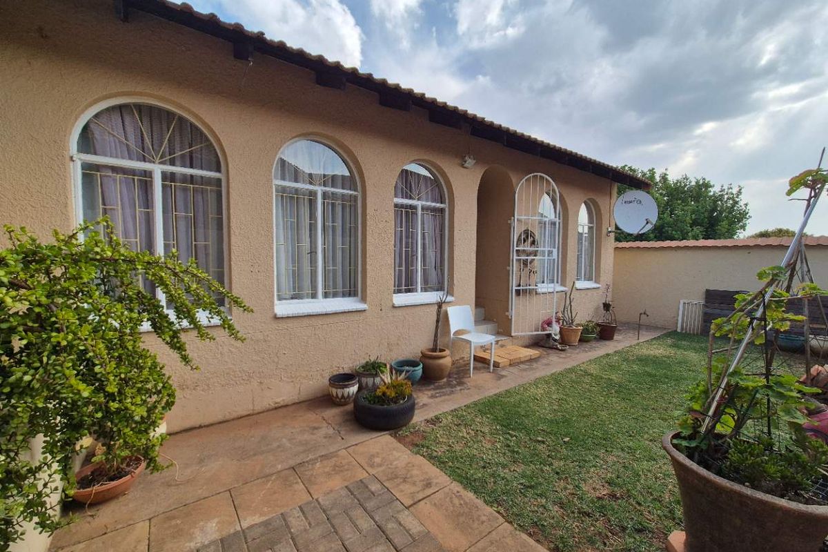 Rear view of the townhouse featuring arched windows, a paved patio area, and a small garden space.