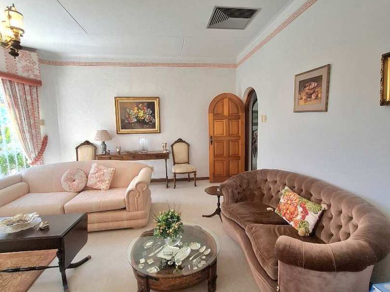 A spacious living room featuring traditional architectural details, including an arched wooden door, decorative coving, and a neutral carpeted floor.