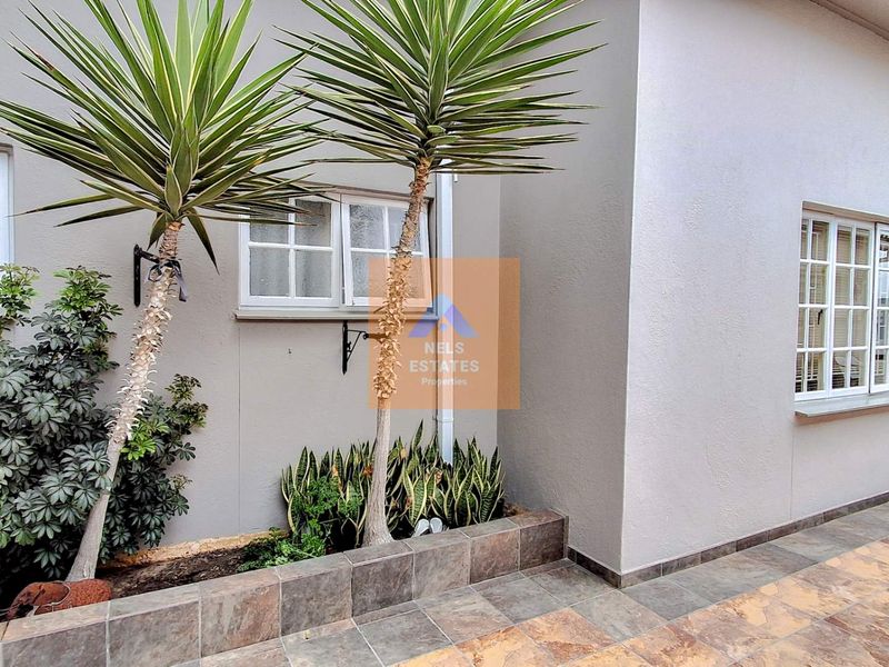 A neat rear exterior area featuring a tiled patio, raised garden bed with established plants, and white-framed casement windows.
