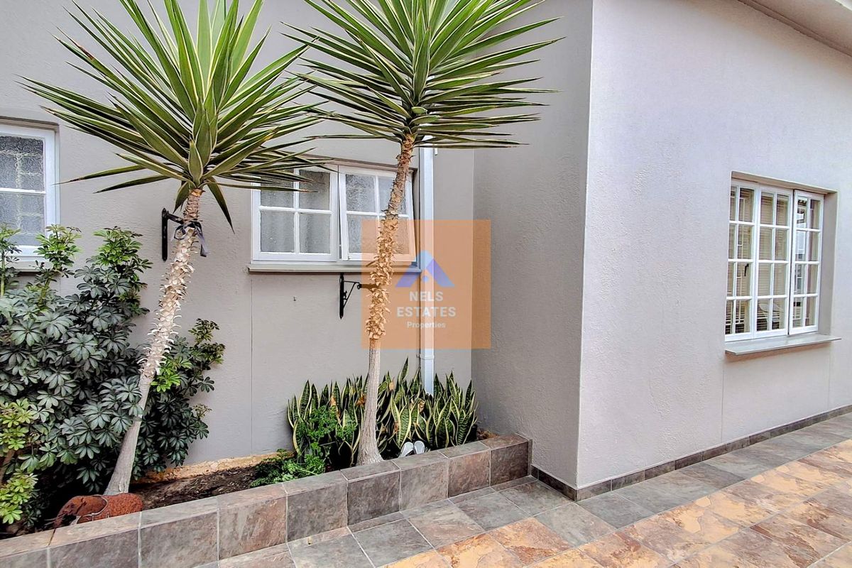 A neat rear exterior area featuring a tiled patio, raised garden bed with established plants, and white-framed casement windows.
