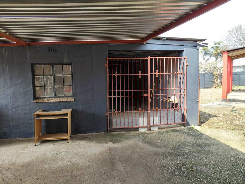 A detached garage structure featuring a corrugated metal roof, steel security gate, and a concrete driveway area.