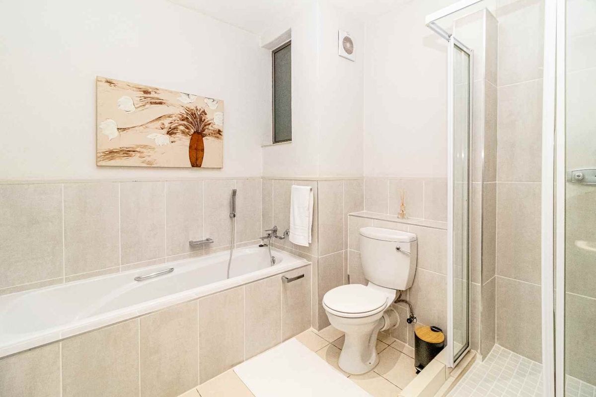 A clean, modern bathroom featuring a bathtub, separate shower enclosure, and toilet with neutral wall and floor tiling.
