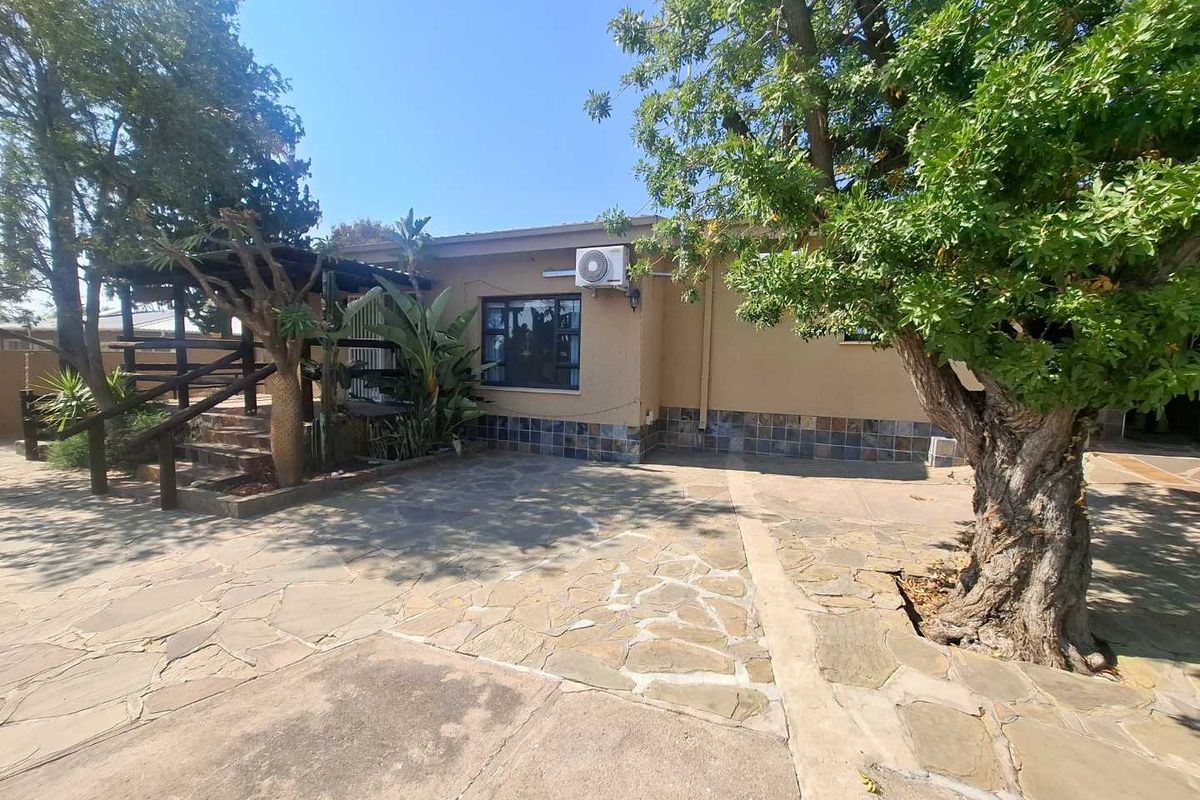 Rear exterior view of the property featuring stone paving, a wooden deck area, and mature landscaping.