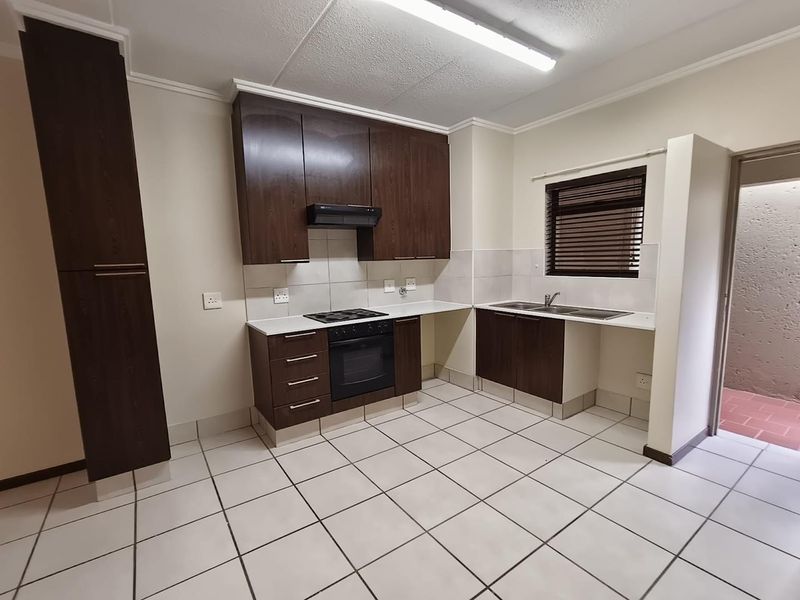 A functional kitchen featuring dark wood cabinetry, built-in oven with hob, extractor fan, double sink, and tiled flooring throughout.