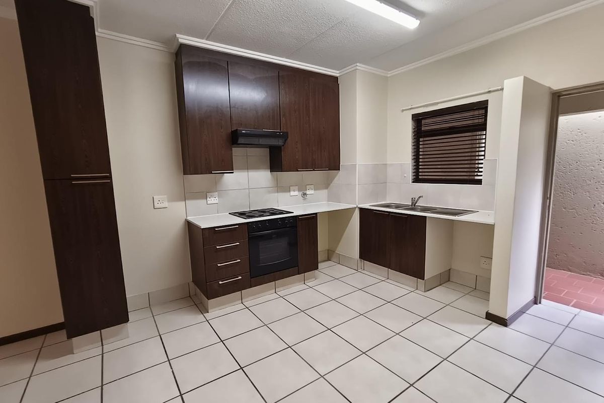 A functional kitchen featuring dark wood cabinetry, built-in oven with hob, extractor fan, double sink, and tiled flooring throughout.