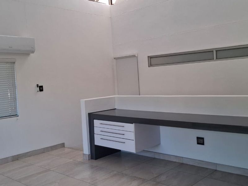 A clean, modern home office space featuring a built-in desk, tiled flooring, split-system air conditioning, and clerestory windows for natural light.