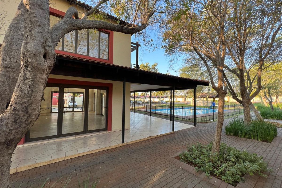 Rear view of the apartment featuring a covered tiled patio, paved walkways, and access to a communal swimming pool area.