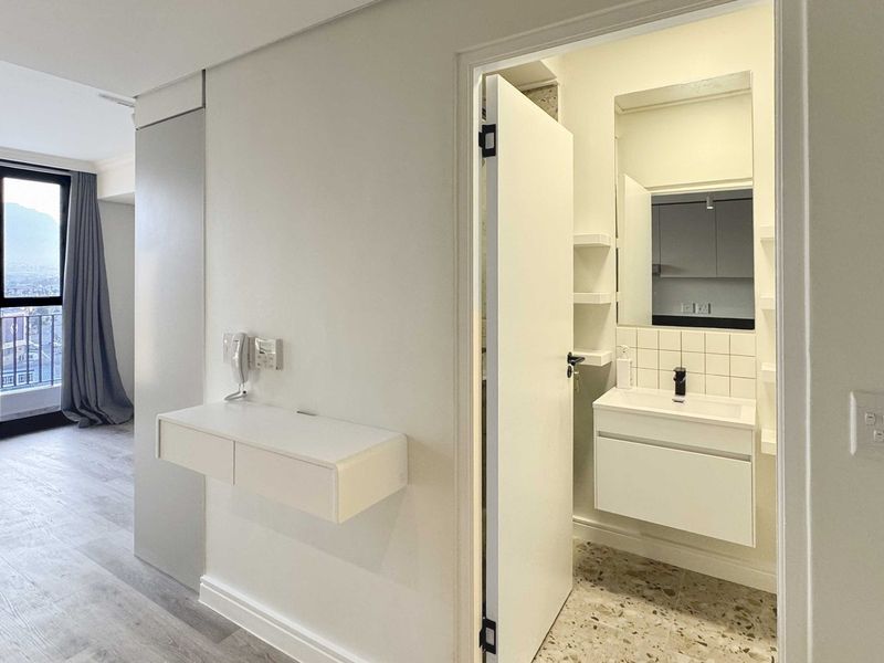 A modern, minimalist bathroom featuring a wall-mounted vanity, basin, and stylish terrazzo flooring, adjacent to a bright living area with balcony access.