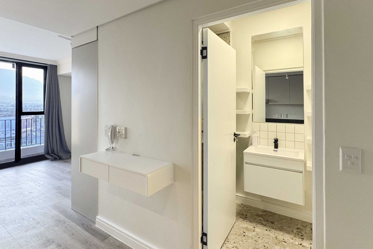 A modern, minimalist bathroom featuring a wall-mounted vanity, basin, and stylish terrazzo flooring, adjacent to a bright living area with balcony access.