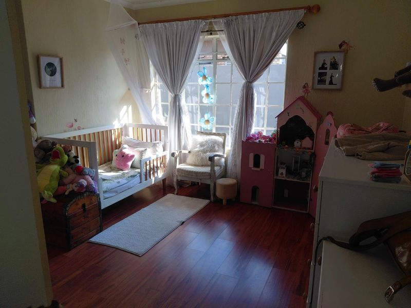 A bedroom featuring laminate flooring and a large window with security bars, currently utilized as a child's room.