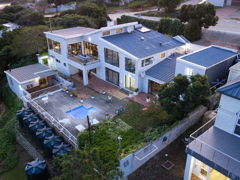 Aerial view of a multi-level guest house featuring a swimming pool, timber deck, paved patio areas, and multiple water storage tanks.