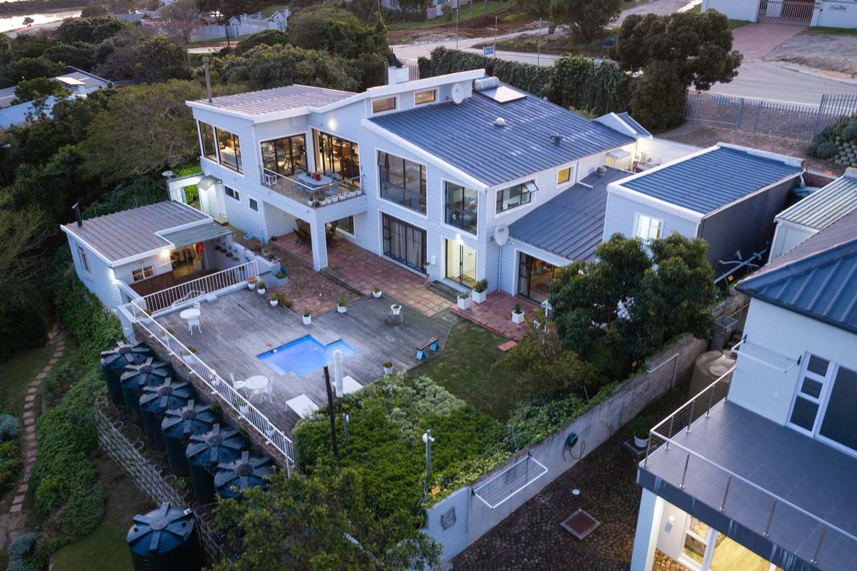 Aerial view of a multi-level guest house featuring a swimming pool, timber deck, paved patio areas, and multiple water storage tanks.