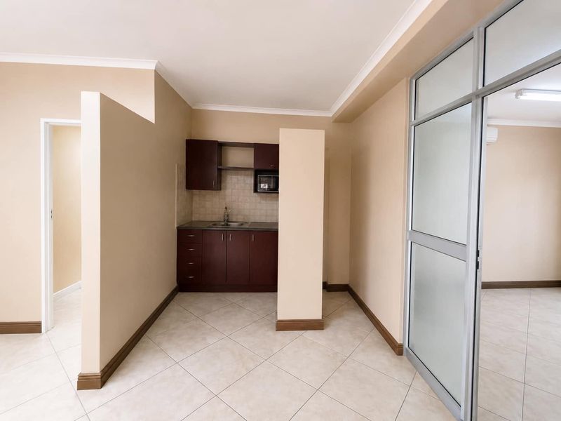 A compact, well-maintained kitchenette featuring dark wood cabinetry, a stainless steel sink, and tiled flooring, separated by an aluminium and glass partition.
