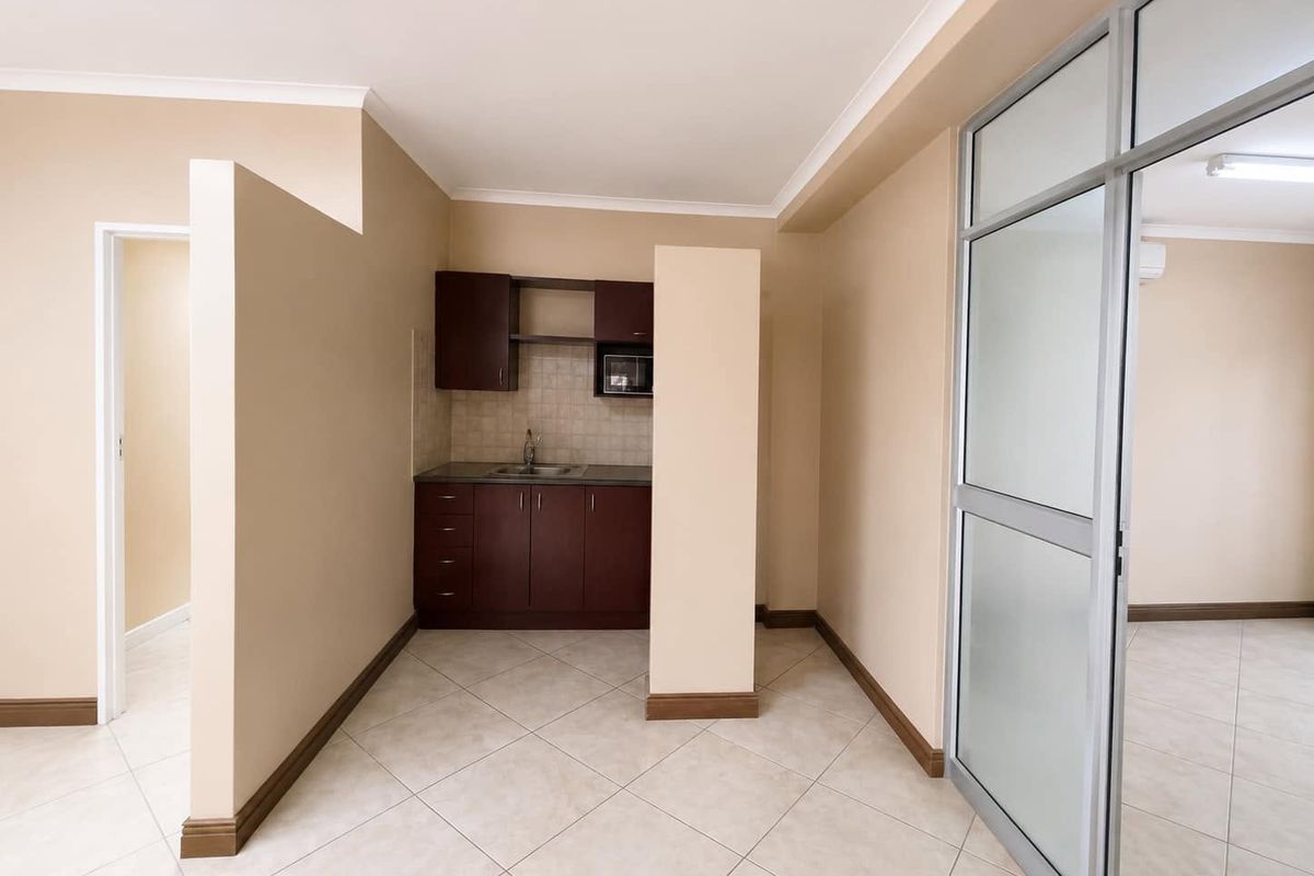 A compact, well-maintained kitchenette featuring dark wood cabinetry, a stainless steel sink, and tiled flooring, separated by an aluminium and glass partition.