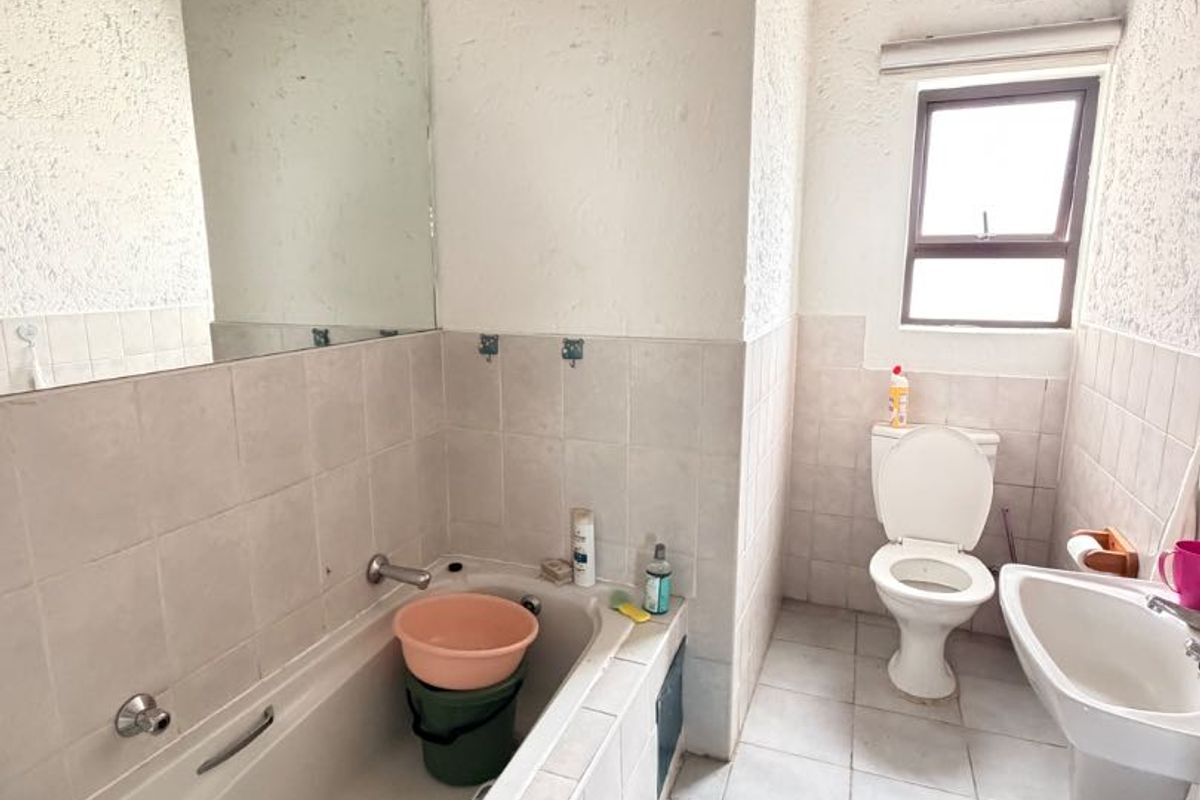A dated bathroom featuring a built-in bathtub, pedestal basin, and toilet with tiled finishes, requiring cosmetic updates to improve its overall condition.