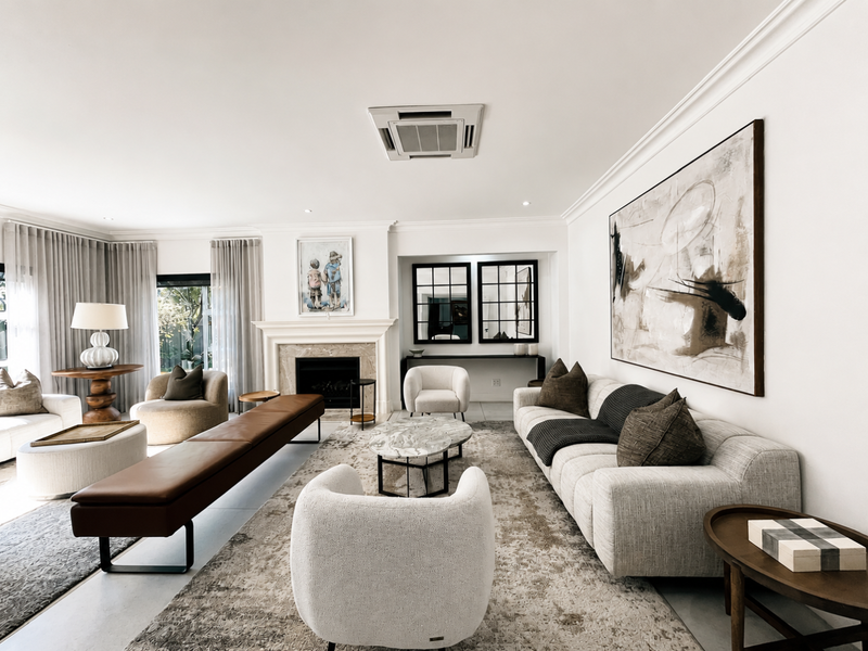 A spacious and elegantly appointed living room featuring a classic fireplace, crown molding, and integrated ceiling air conditioning, offering a refined and comfortable atmosphere.