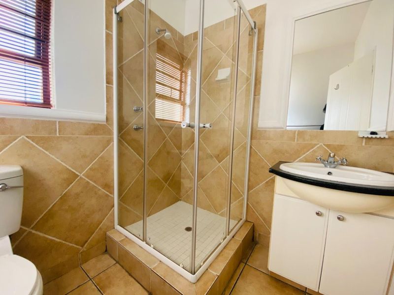 A functional bathroom featuring a corner shower enclosure, vanity cabinet with basin, wall mirror, and neutral tiled finishes throughout.