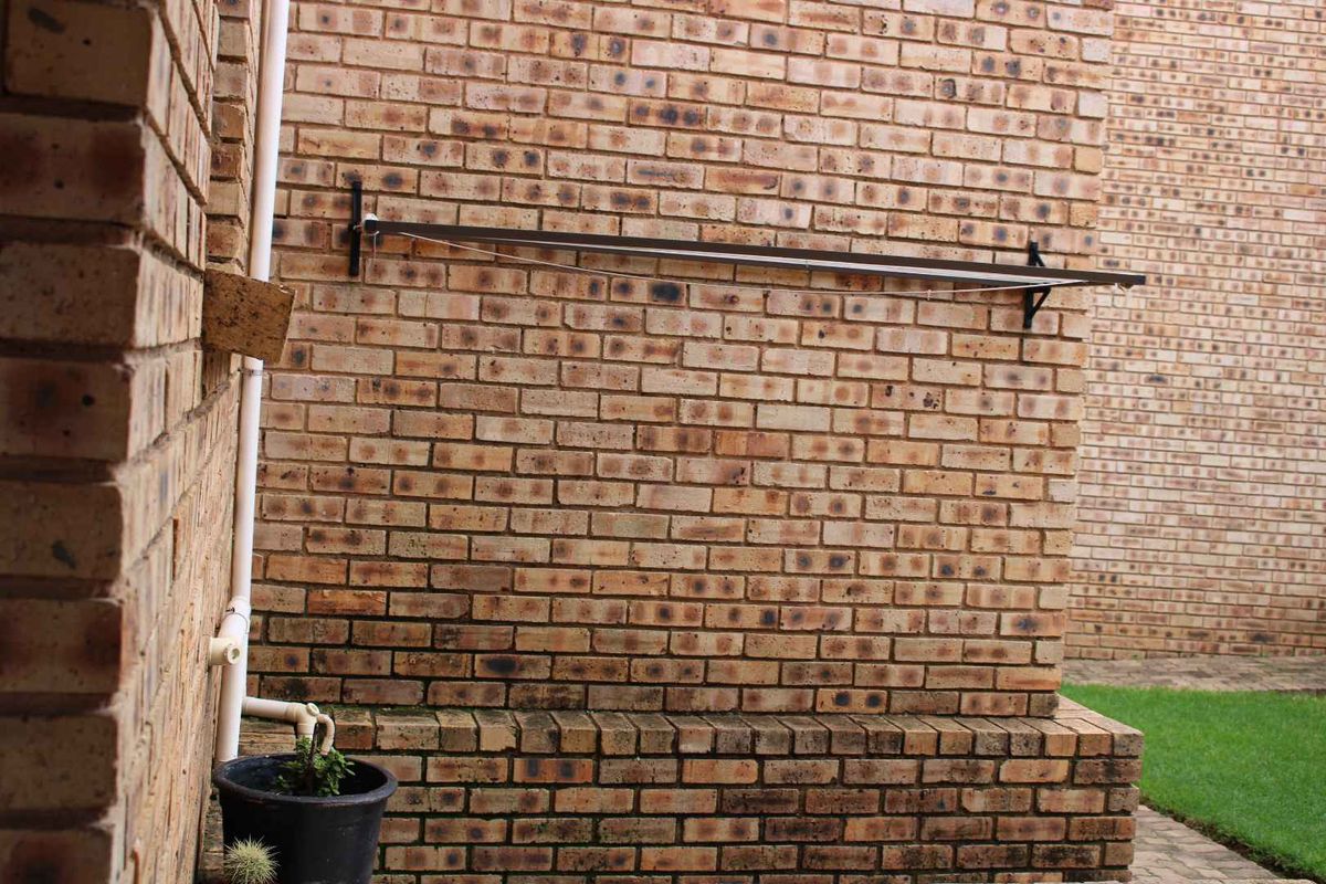 A rear exterior view of the townhouse featuring a face brick wall with a mounted washing line and a brick plinth.