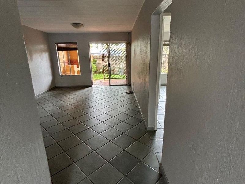 An empty, open-plan living area featuring neutral tiled flooring, flush mount lighting, and a sliding glass door providing access to the rear garden.