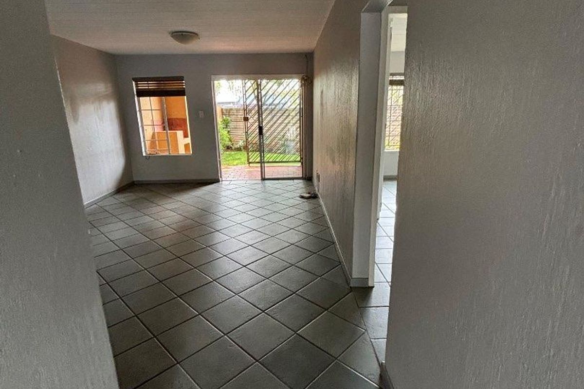 An empty, open-plan living area featuring neutral tiled flooring, flush mount lighting, and a sliding glass door providing access to the rear garden.