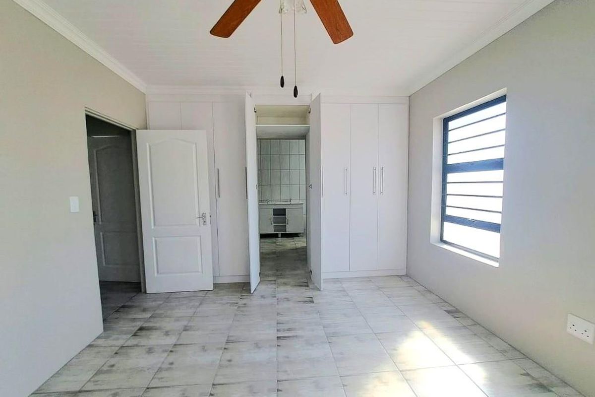 A spacious, empty bedroom featuring built-in cupboards, tiled flooring, a ceiling fan, and a view through to an adjacent tiled utility area.