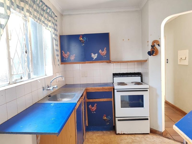 A dated kitchen featuring blue cabinetry, a tiled backsplash, and a freestanding stove, offering significant potential for a modern renovation.