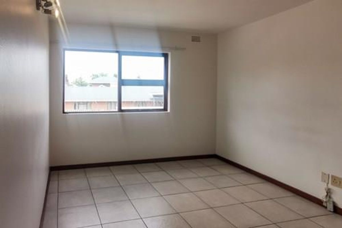 A clean, empty bedroom featuring neutral tiled flooring, a large aluminium-framed window, and simple wall-mounted lighting, ready for personalization.