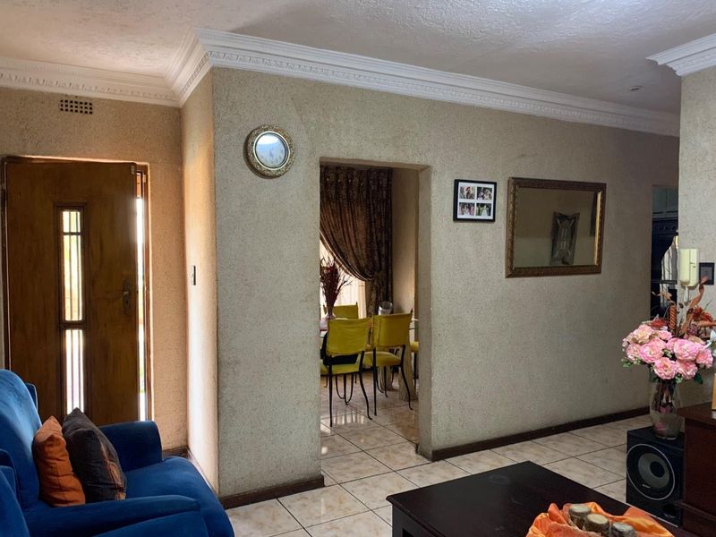 Living room area featuring ceramic floor tiles, decorative crown molding, and a timber entrance door, leading through to an adjacent dining space.