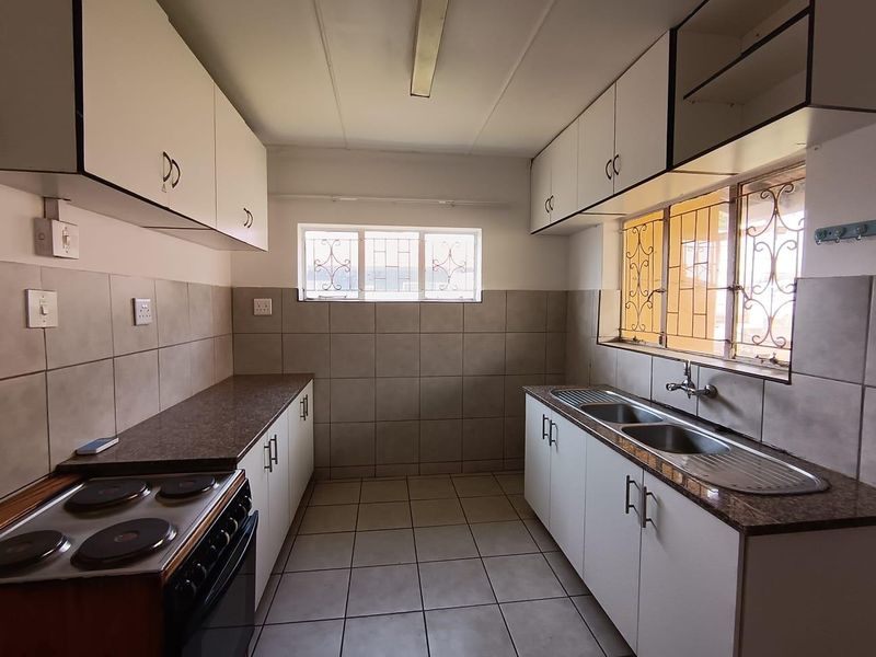A functional kitchen featuring white cabinetry, laminate countertops, a double stainless steel sink, and tiled surfaces throughout, offering a clean and practical workspace.