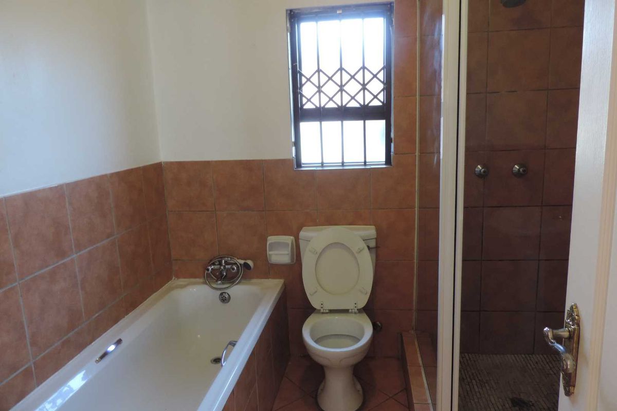 A functional bathroom featuring a built-in bathtub, separate shower enclosure, and toilet, finished with mid-tone ceramic wall and floor tiles.