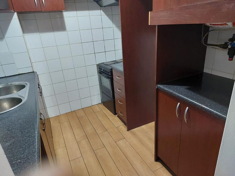 A functional kitchen featuring dark wood-finish cabinetry, laminate countertops, a built-in stove, and tiled splashbacks with wood-look flooring.