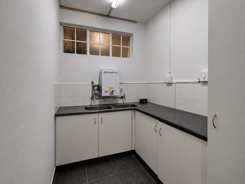 A functional kitchenette featuring built-in cabinetry, a double sink, laminate countertops, and a wall-mounted water heater in a clean, tiled space.