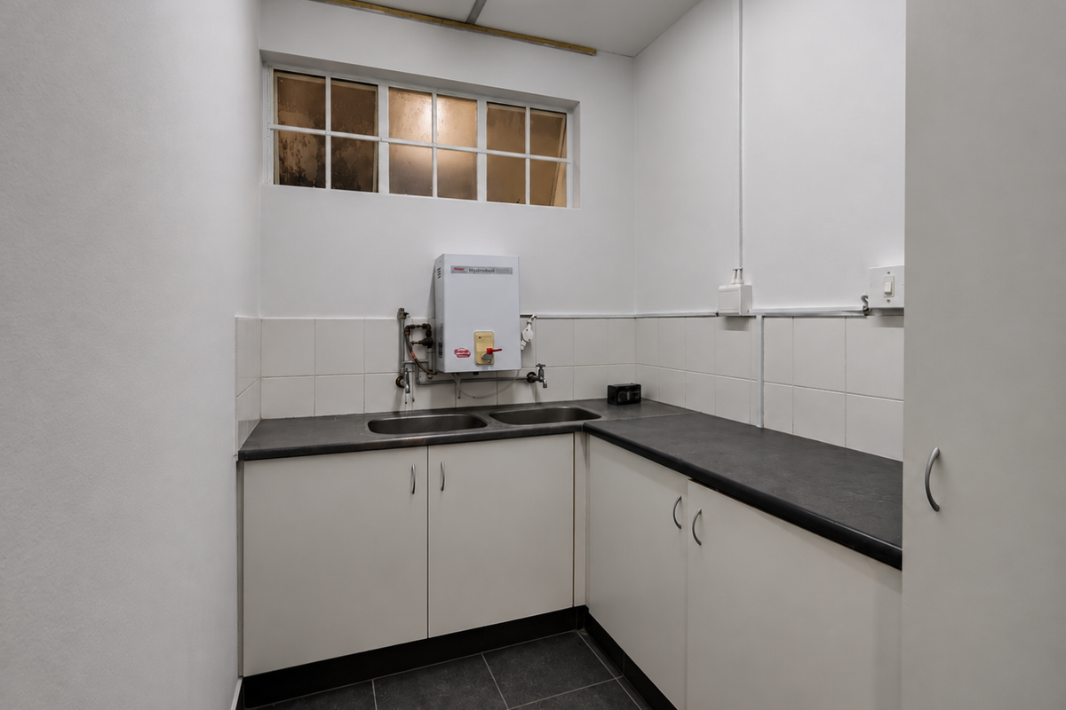 A functional kitchenette featuring built-in cabinetry, a double sink, laminate countertops, and a wall-mounted water heater in a clean, tiled space.