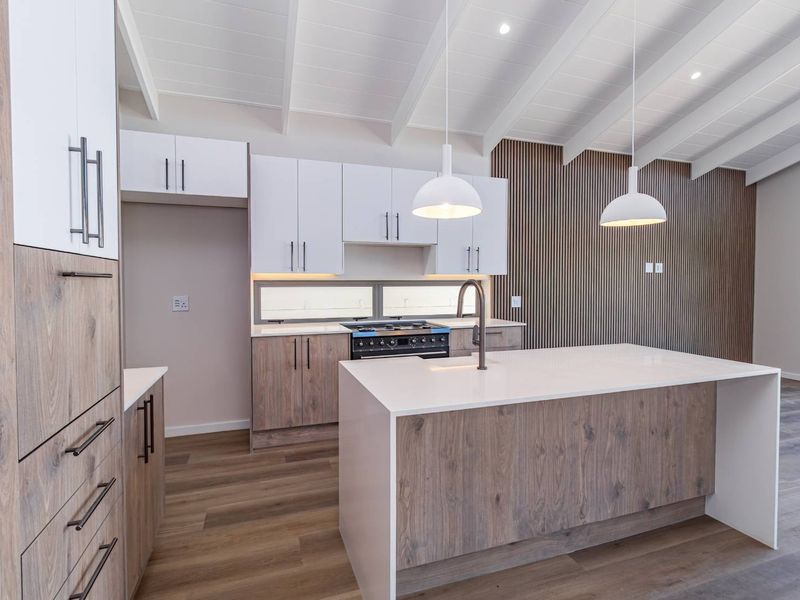 Modern kitchen featuring a central island, two-tone cabinetry, gas stove, and a striking slatted wood feature wall under an exposed beam ceiling.