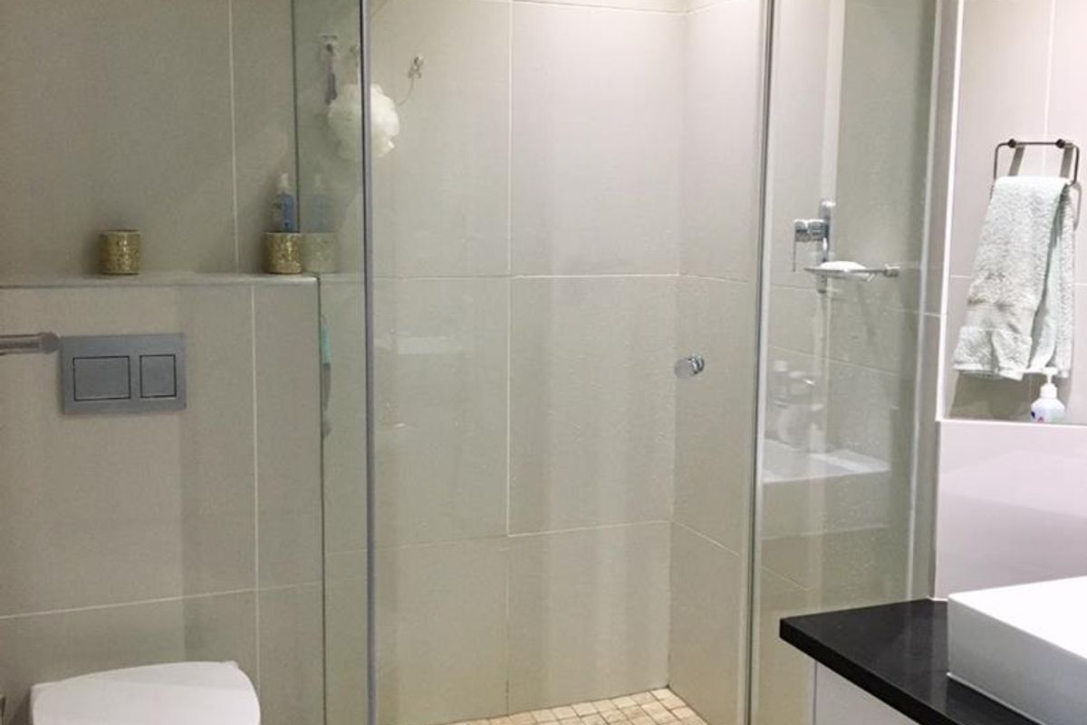 Modern bathroom featuring a glass-enclosed shower, wall-mounted toilet, and a vanity with a countertop basin, finished with neutral wall tiles.