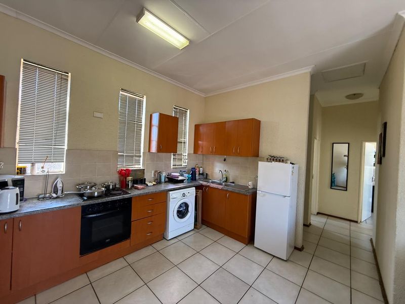 Functional kitchen featuring wood-finish cabinetry, tiled flooring, built-in oven and hob, and integrated laundry plumbing, offering a practical layout for daily use.
