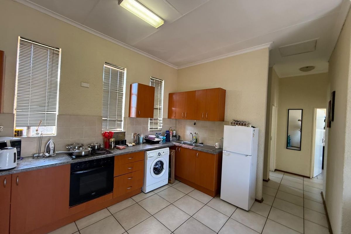 Functional kitchen featuring wood-finish cabinetry, tiled flooring, built-in oven and hob, and integrated laundry plumbing, offering a practical layout for daily use.