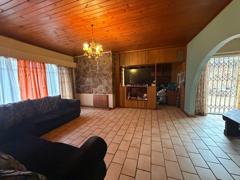 Spacious living room featuring a timber-clad ceiling, stone feature wall, built-in cabinetry, and tiled flooring, leading to an outdoor area through a security gate.