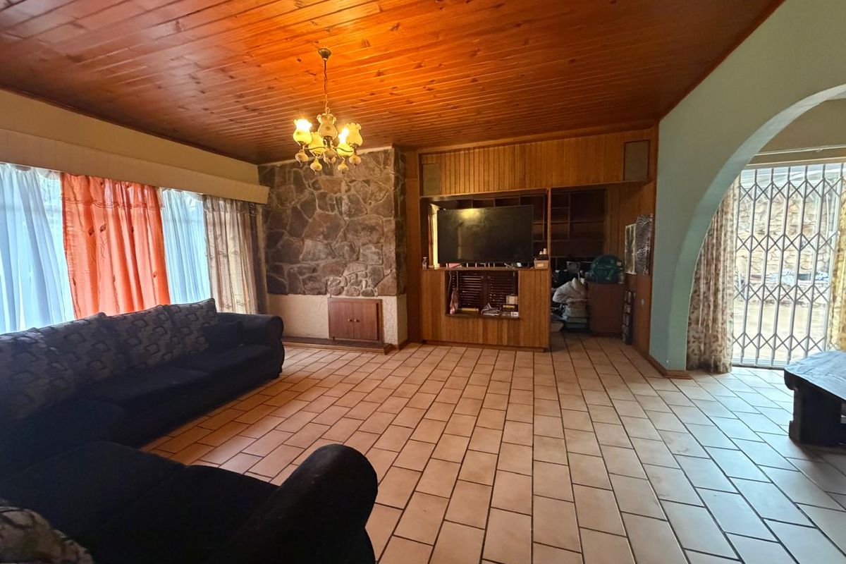 Spacious living room featuring a timber-clad ceiling, stone feature wall, built-in cabinetry, and tiled flooring, leading to an outdoor area through a security gate.