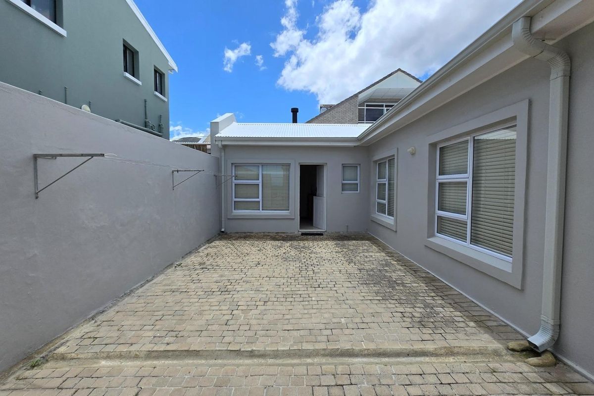 A private rear courtyard featuring paved flooring, exterior wall-mounted drying racks, and access to the main dwelling through a central doorway.