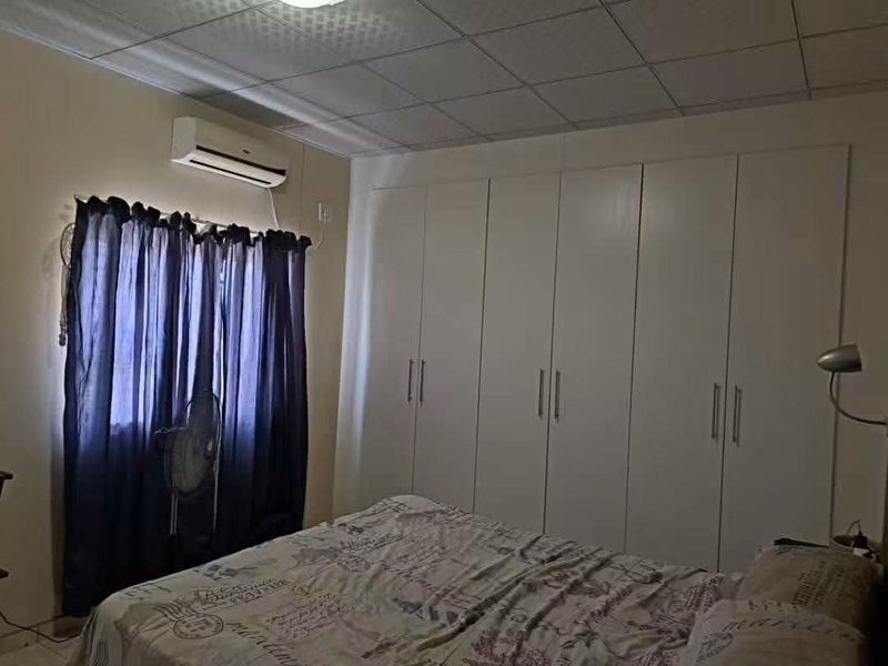 A bedroom featuring extensive built-in cupboards, a split-system air conditioner, and a tiled ceiling finish.