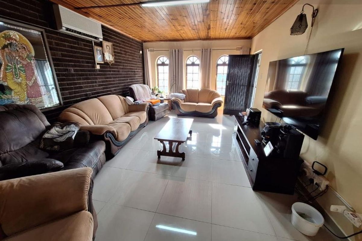 Spacious living room featuring a timber ceiling, exposed brick wall, tiled flooring, and large arch-top windows providing natural light.